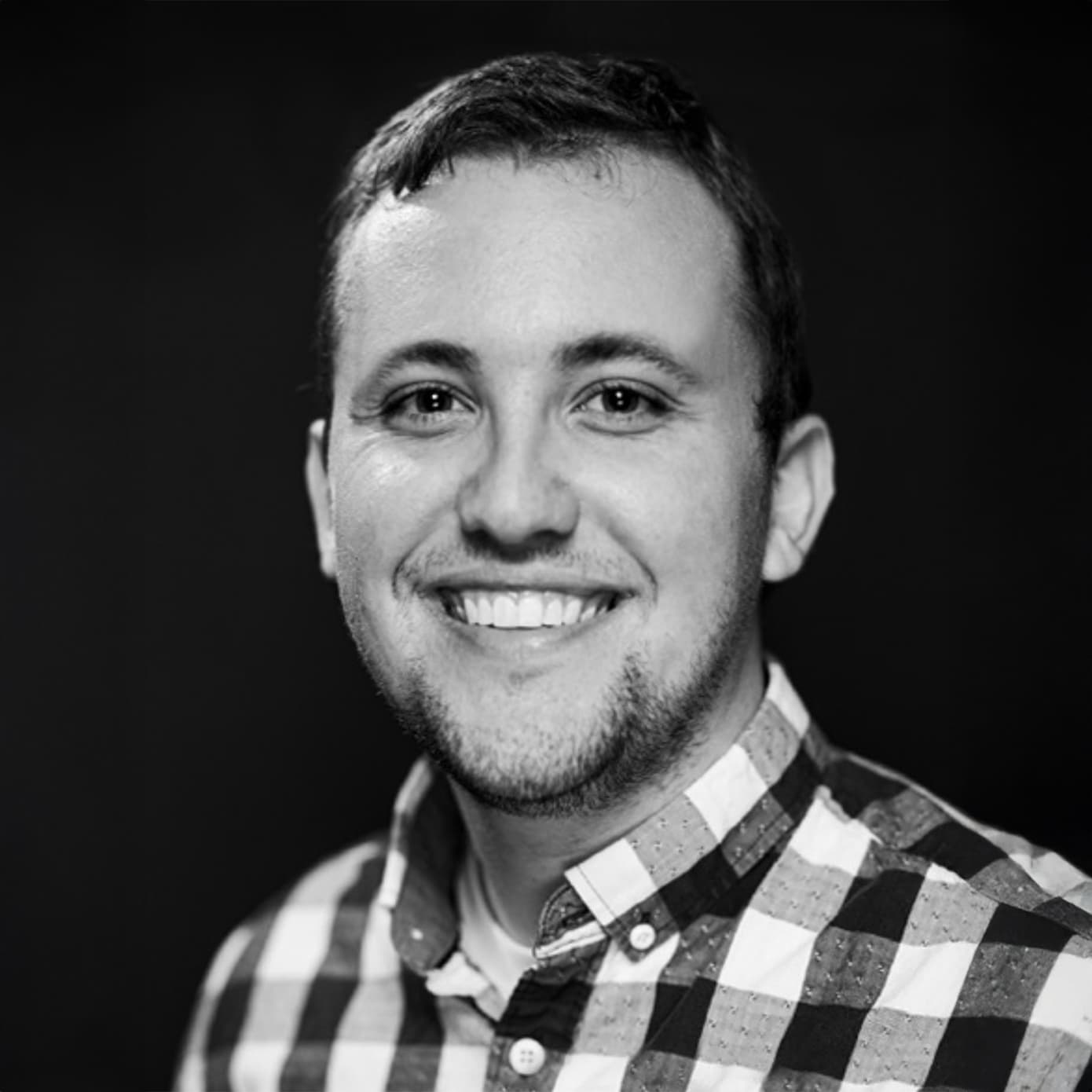 Ty Pleban, in a black and white portrait, wearing a checked shirt.